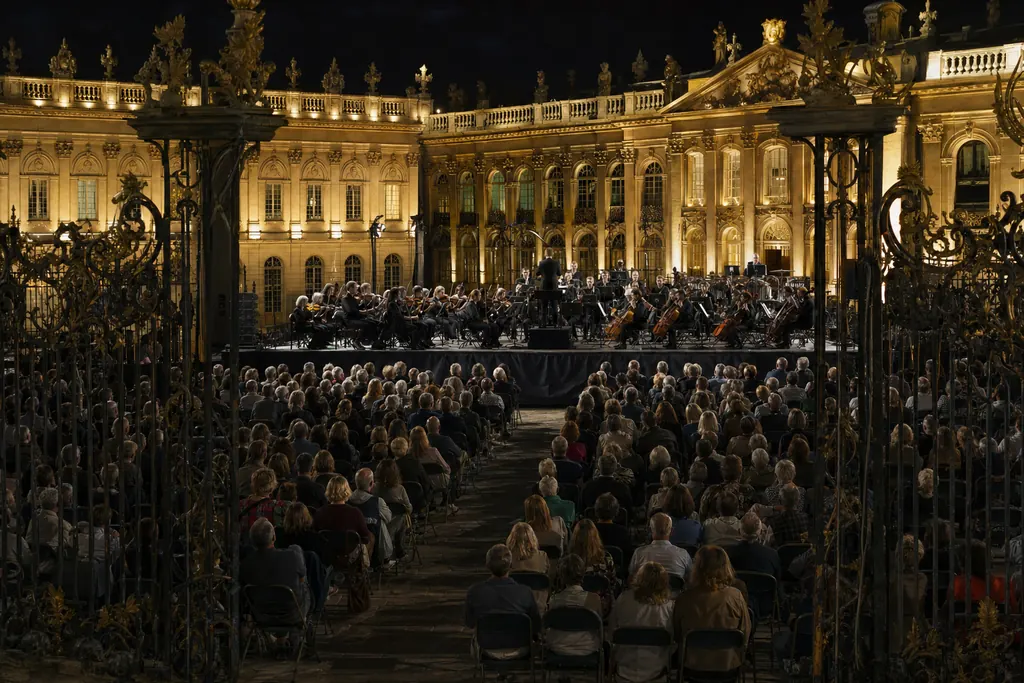 Orchestra su un palco all'aperto in una piazza di palazzo, con cancellata in ferro battuto (immagine creata con AI)