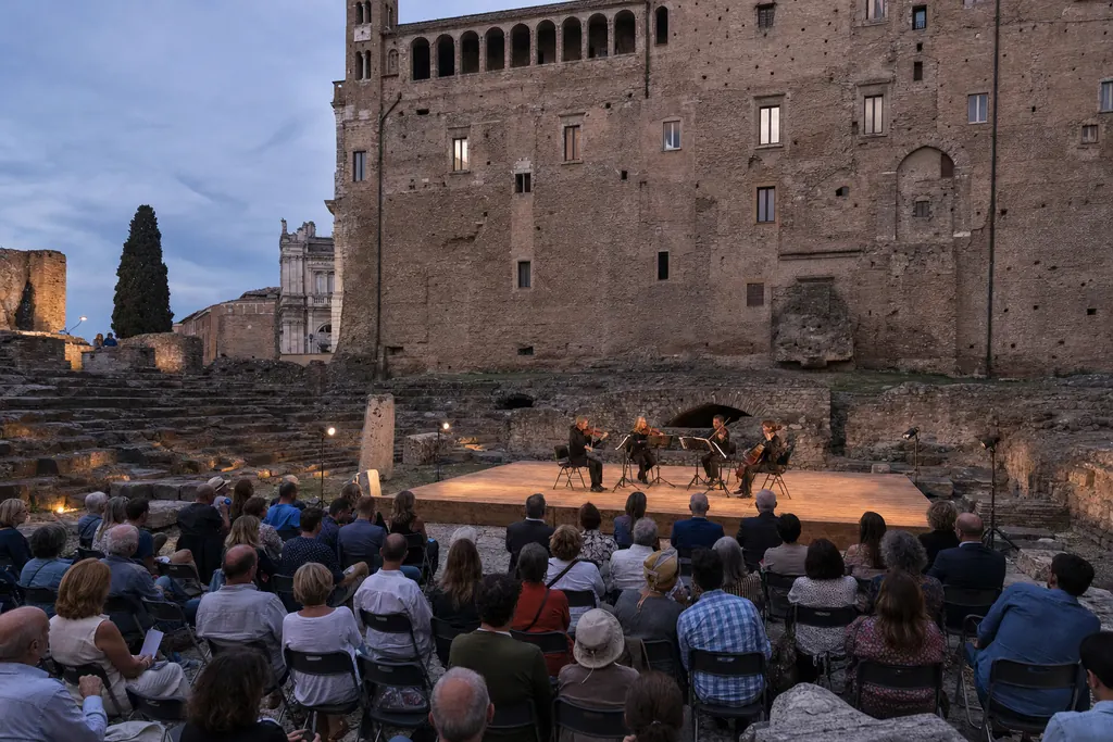 Concerto serale tra le rovine di un teatro romano, pubblico di spalle e luci calde (immagine creata con AI)