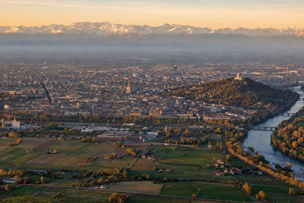 Veduta aerea di Torino al tramonto con il Po, la collina di Superga e le Alpi innevate all'orizzonte (immagine creata con AI)