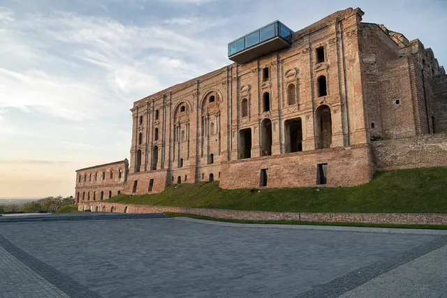 Facciata incompiuta in mattoni di una residenza barocca in collina con belvedere moderno in vetro (immagine creata con AI)