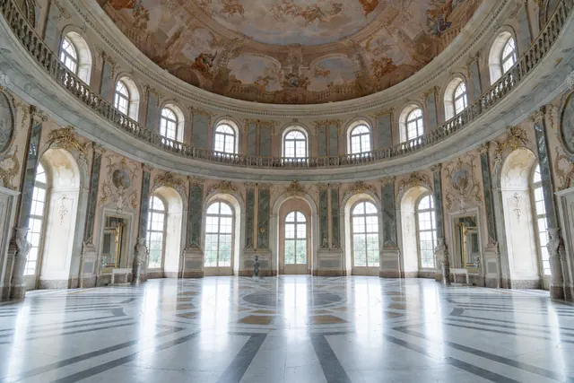 Grande salone ovale barocco con cupola affrescata, finestre ad arco e pavimento in marmo (immagine creata con AI)
