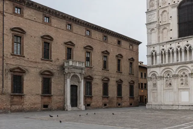 Facciata in mattoni di un palazzo storico affacciato su una piazza lastricata accanto a una cattedrale (immagine creata con AI)